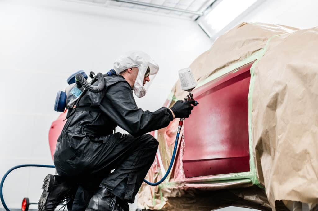 Ein Lackierer bei Autohaus Lang lackiert ein rotes Fahrzeug in der neuen Lackierkabine