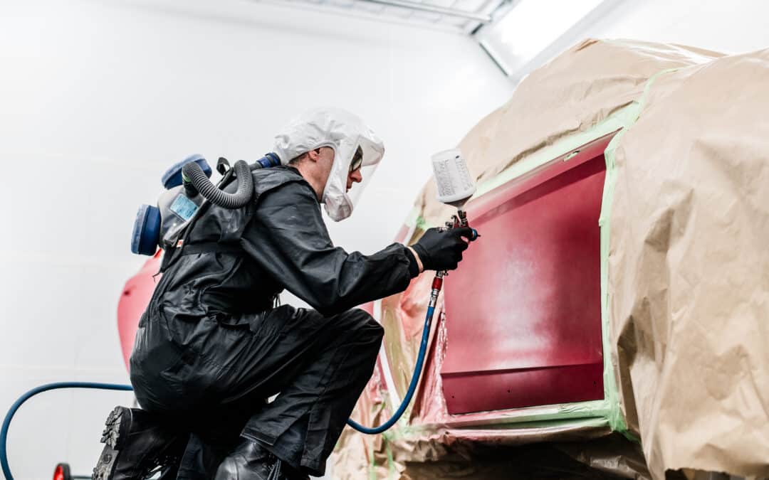 Ein Lackierer bei Autohaus Lang lackiert ein rotes Fahrzeug in der neuen Lackierkabine