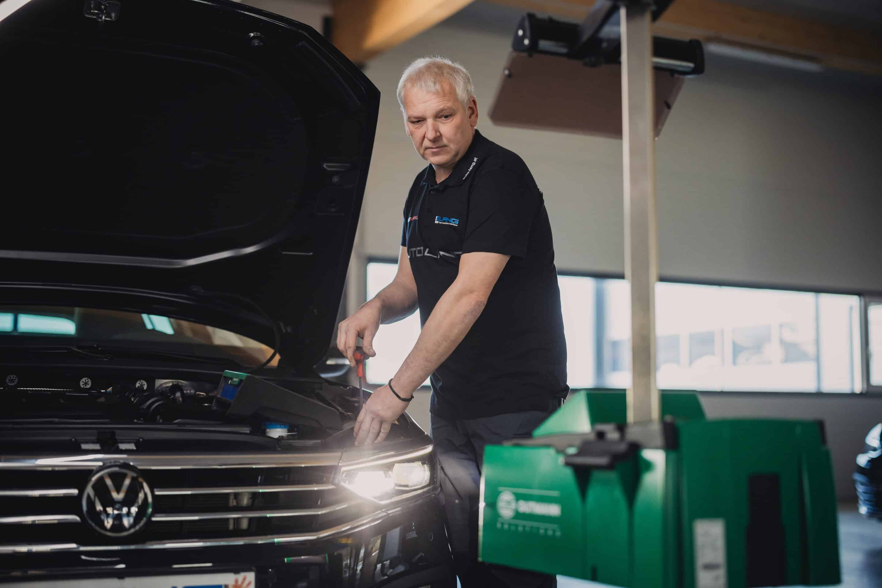 Ein Mechaniker in der Werkstatt von Auto Lang beim Scheinwerfer einstellen eines Scheinwerfers von einem VW